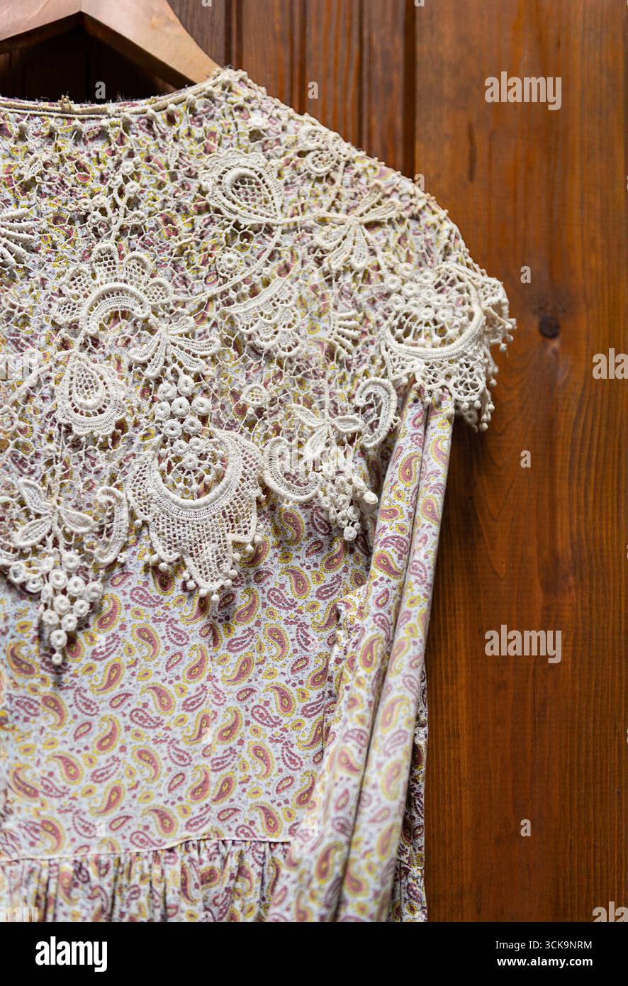 Das altmodische Kleid mit Paisley-Muster hängt am Bügel an der Holzwand Stockfoto