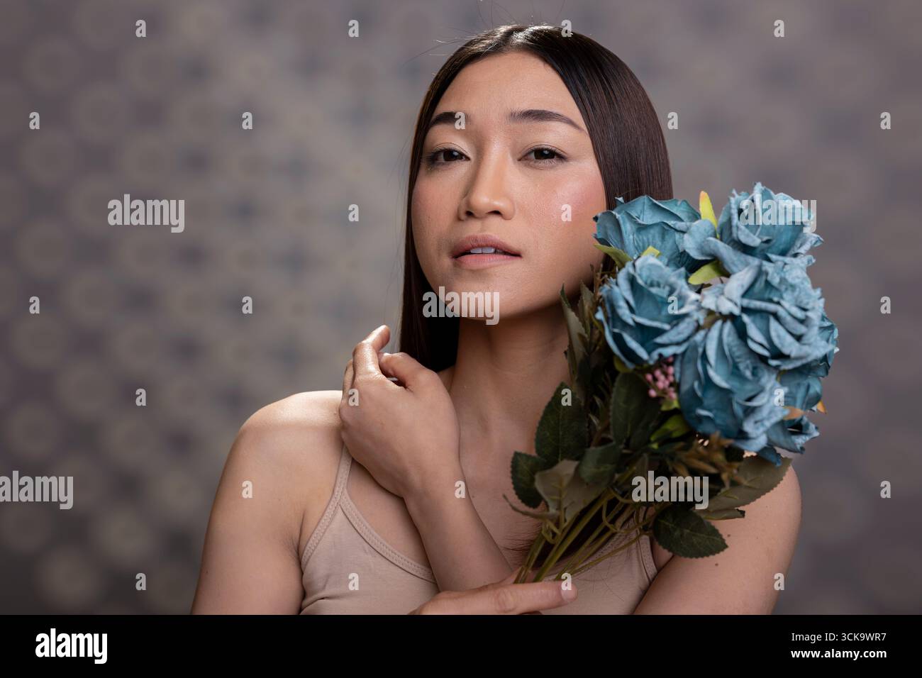 Selbstbewusste Frau mit weicher Haut und natürlichem Make-up-Look hält einen Blumenstrauß blauer Rosen. Frischer strahlender Teint und anmutiger Ausdruck stehen für Selbstpflege und Selbstakzeptanz, Wellness. Stockfoto