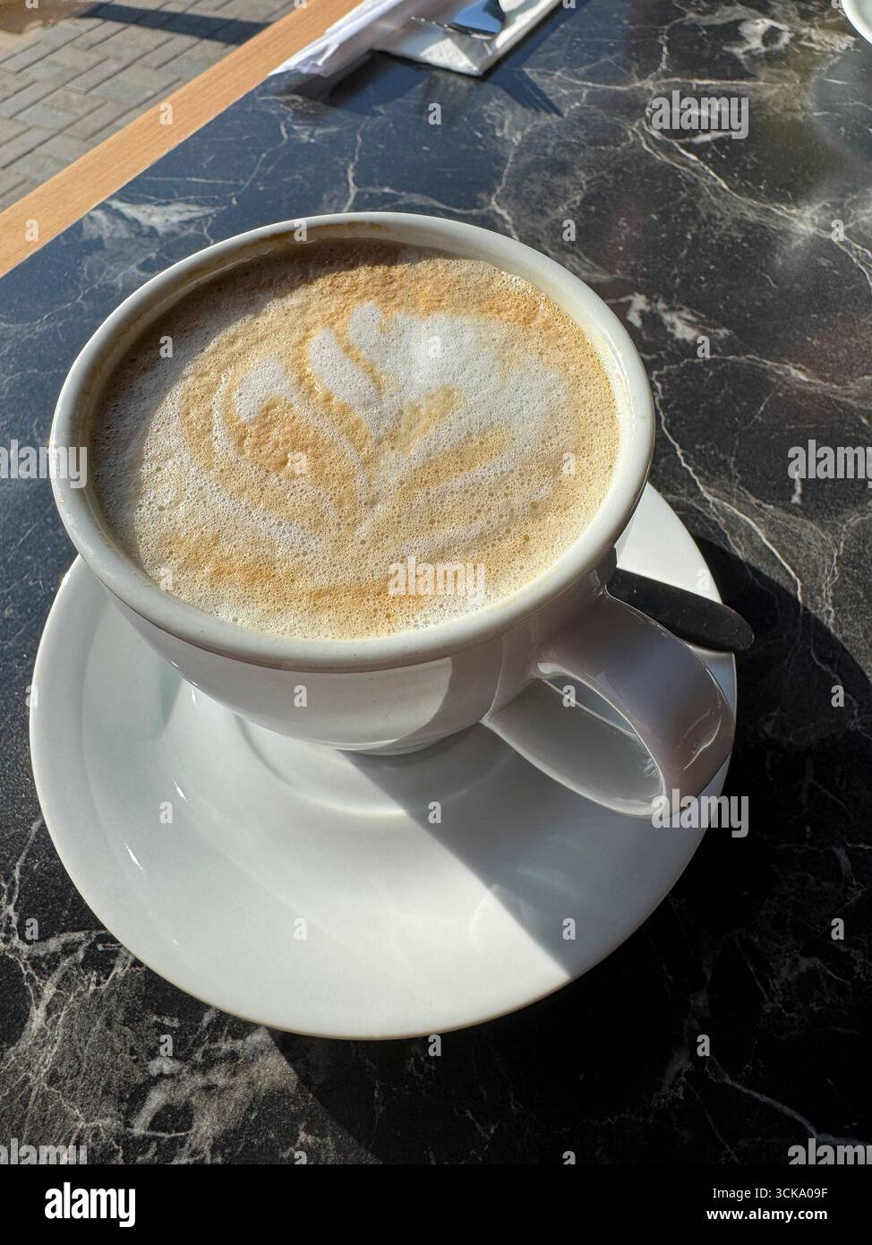 Eine Tasse Cappuccino auf einem Terrassentisch aus schwarzem Marmor Stockfoto
