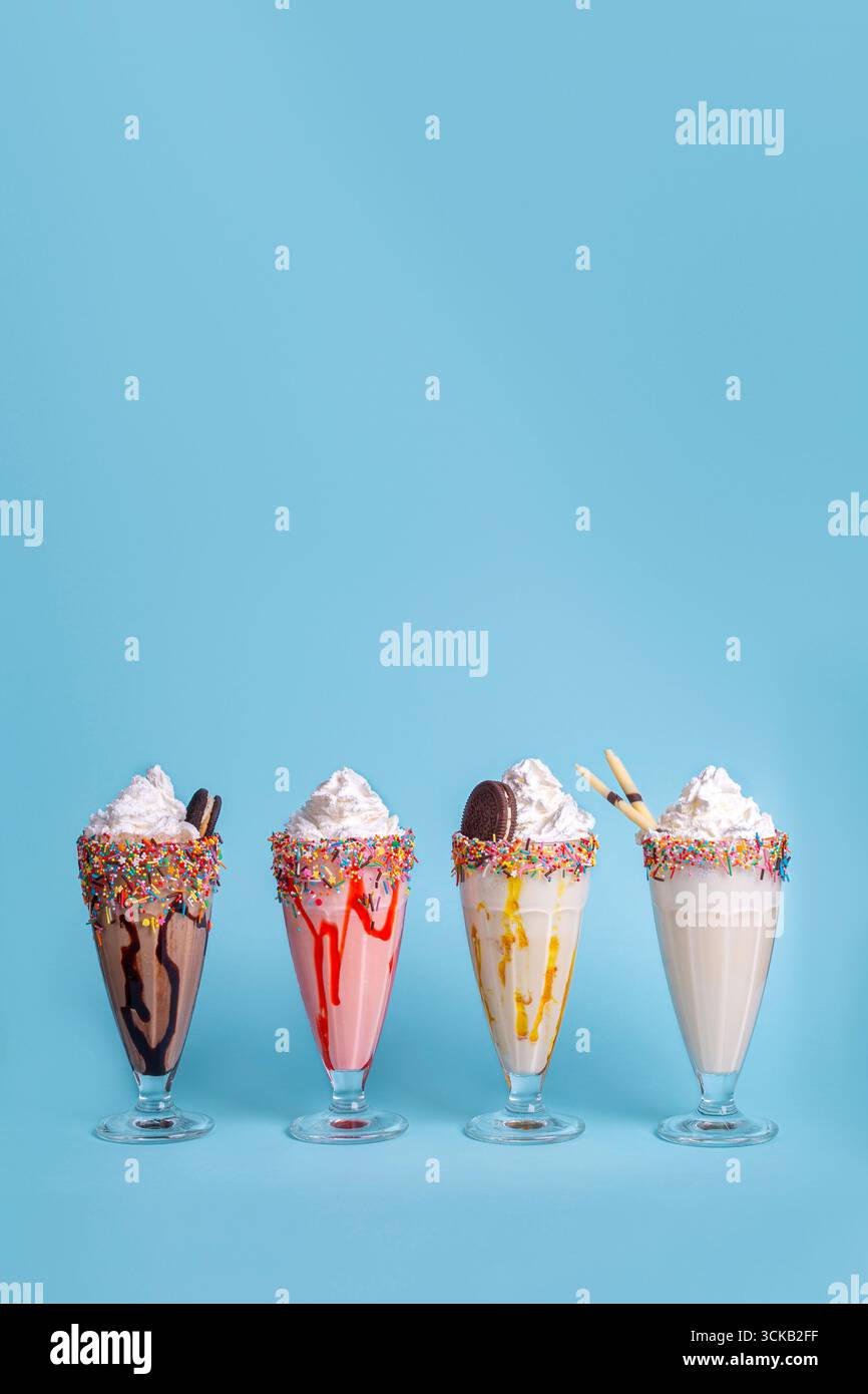 Farbenfrohe Milchshakes in Gläsern auf blauem Hintergrund, erfrischende süße Getränke perfekt für Sommer, Menügestaltung und Lebensmittelwerbung. Stockfoto