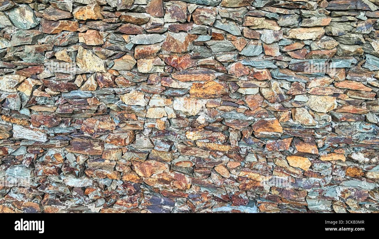 Eine zerklüftete Steinmauer mit unterschiedlich geformten und farbigen flachen Felsen Stockfoto