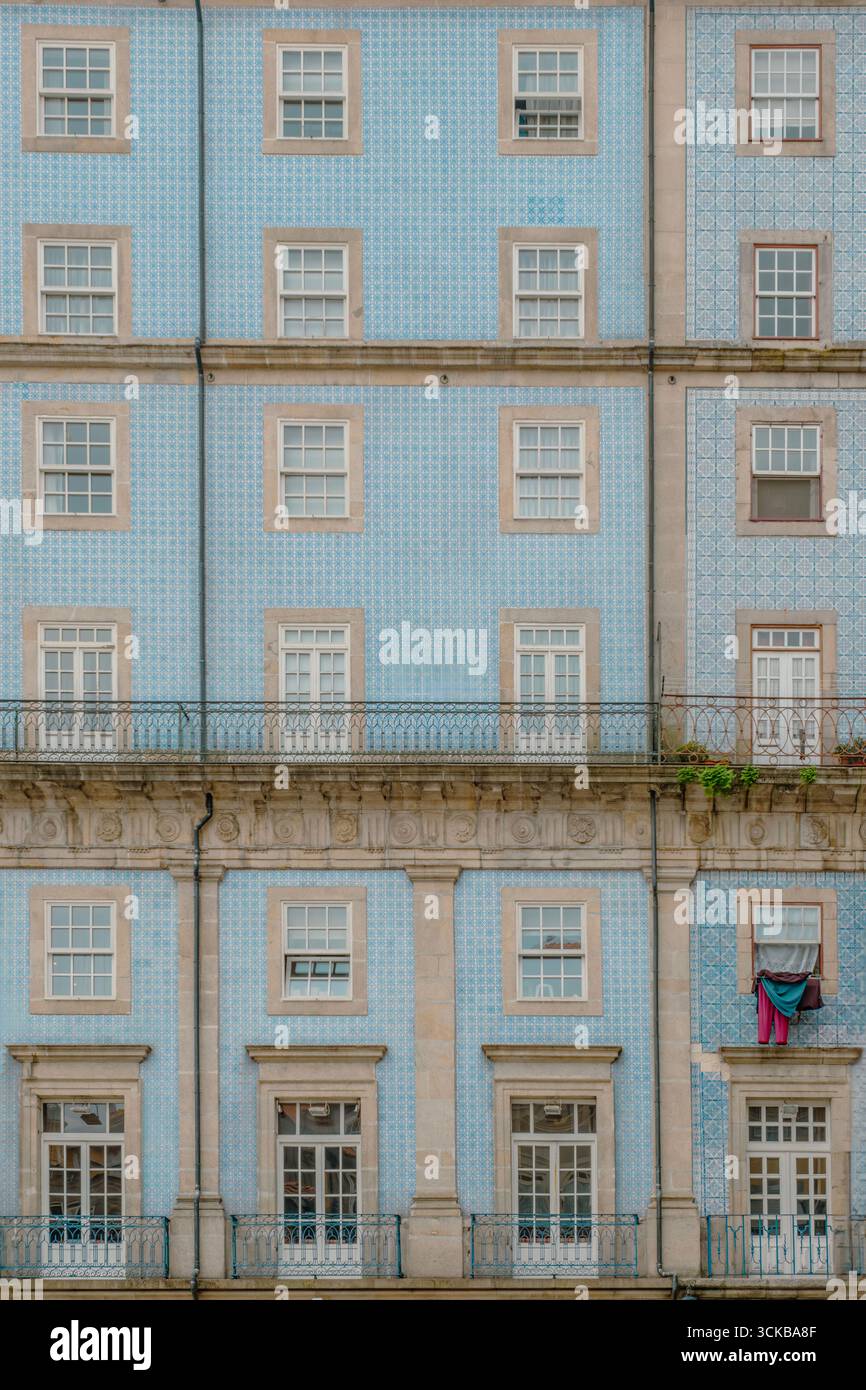 Hellblaue geflieste Fassade mit kunstvollen Balkonen und symmetrischen Fenstern in Porto, Portugal. Dezentes Azulejo-Muster, beigefarbener Steinrahmen, Details für den Alltag Stockfoto