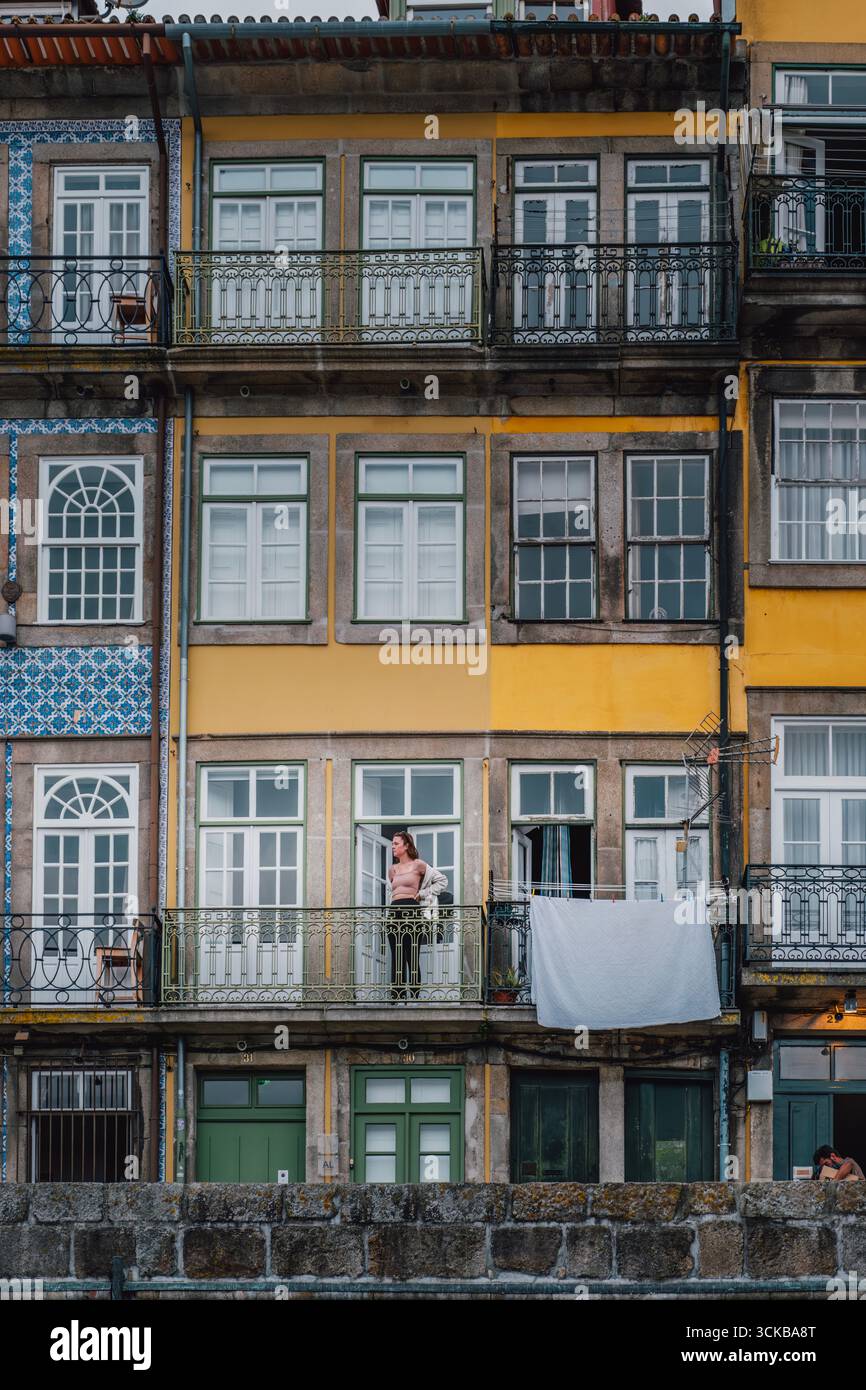 Farbenfrohe mehrteilige Fassade mit Azulejos, gelben Wänden und schmiedeeisernen Balkonen in Porto, Portugal. Jeden Tag, Person auf dem Balkon, Wäscherei hängen Stockfoto