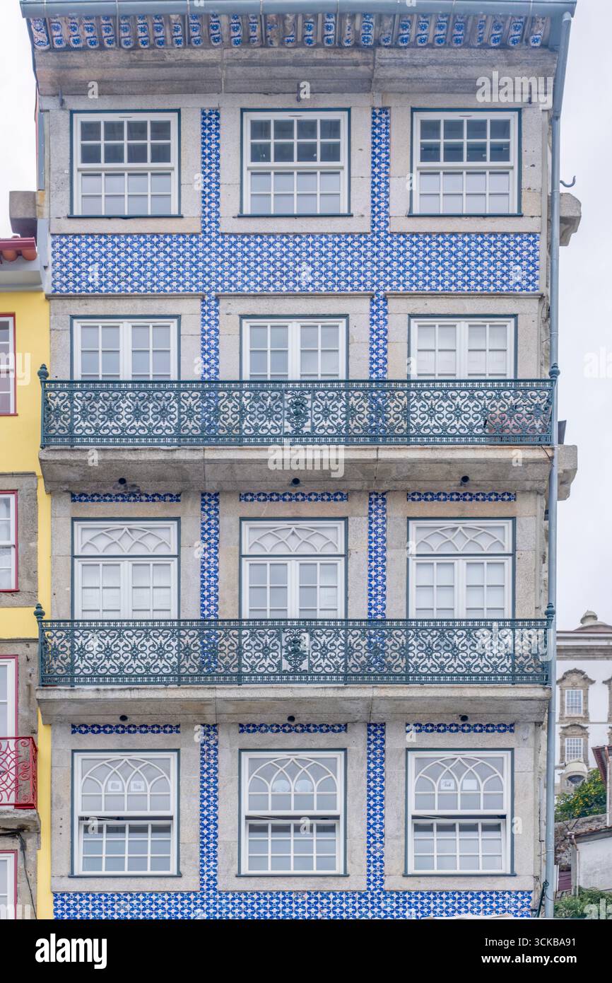 Blau-weiß gekachelte Fassade mit kunstvollen grünen Balkonen und symmetrischen Fenstern in Porto, Portugal. Traditionelles Azulejo-Design, geblümtes Eisen, Urban Stockfoto