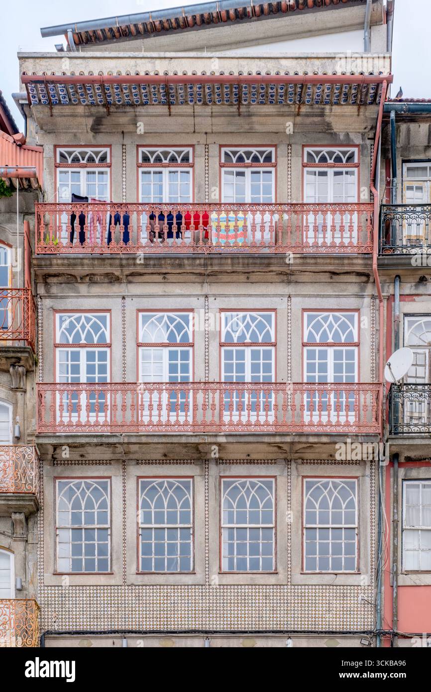 Wohnfassade mit Bogenfenstern, dekorativen Fliesen und Balkon mit hängender Wäscherei in Porto, Portugal. Rotes Geländer, Dachdächer Stockfoto