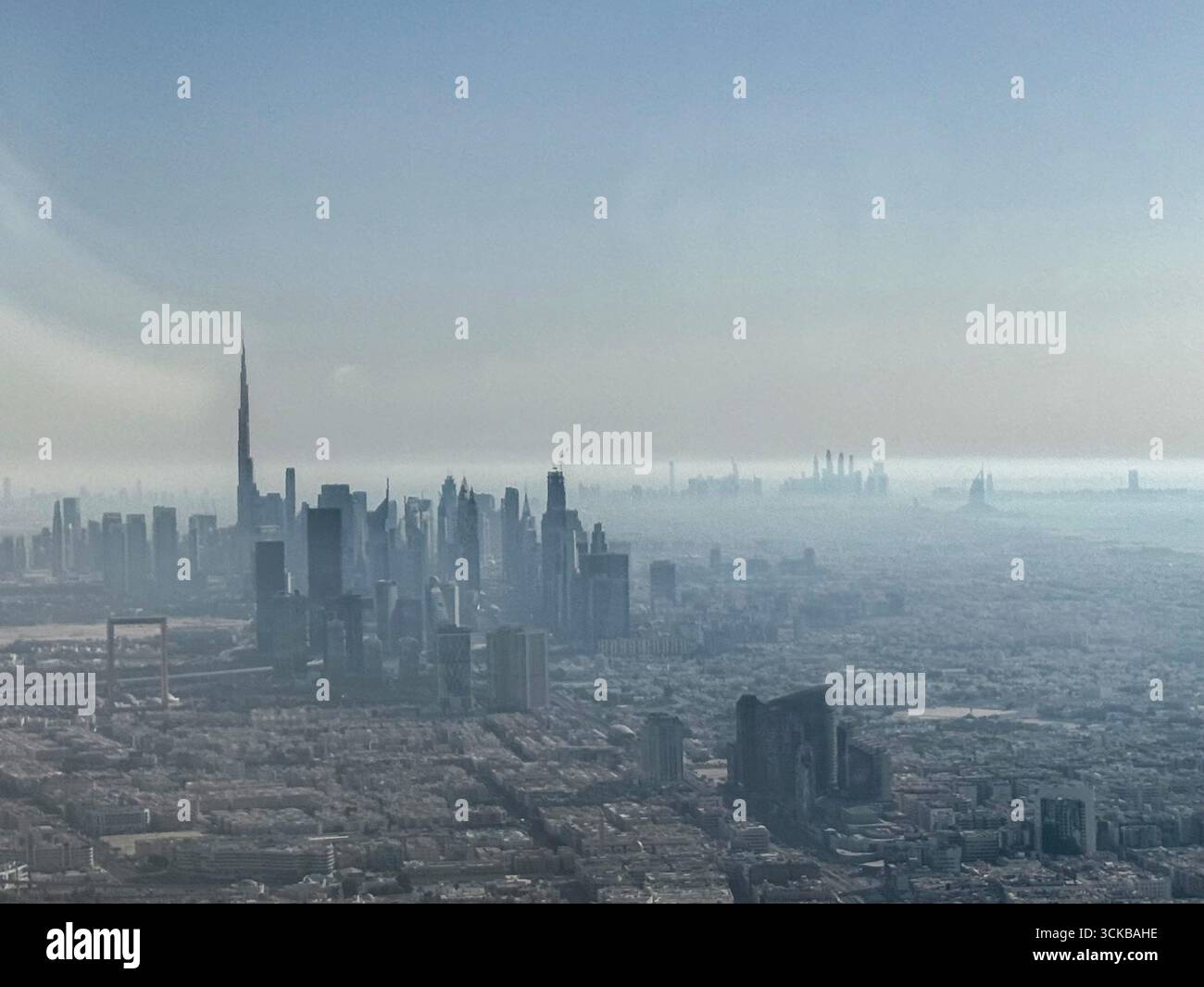 Von einem Fluggastfenster aus in der heißen Distanz befindet sich der bekannte Burj Khalifa Turm, der die Skyline mit einem Komplex gemischter Hochfrequenzanlagen verbindet. - Smartphone-aufgenommenes Stockfoto