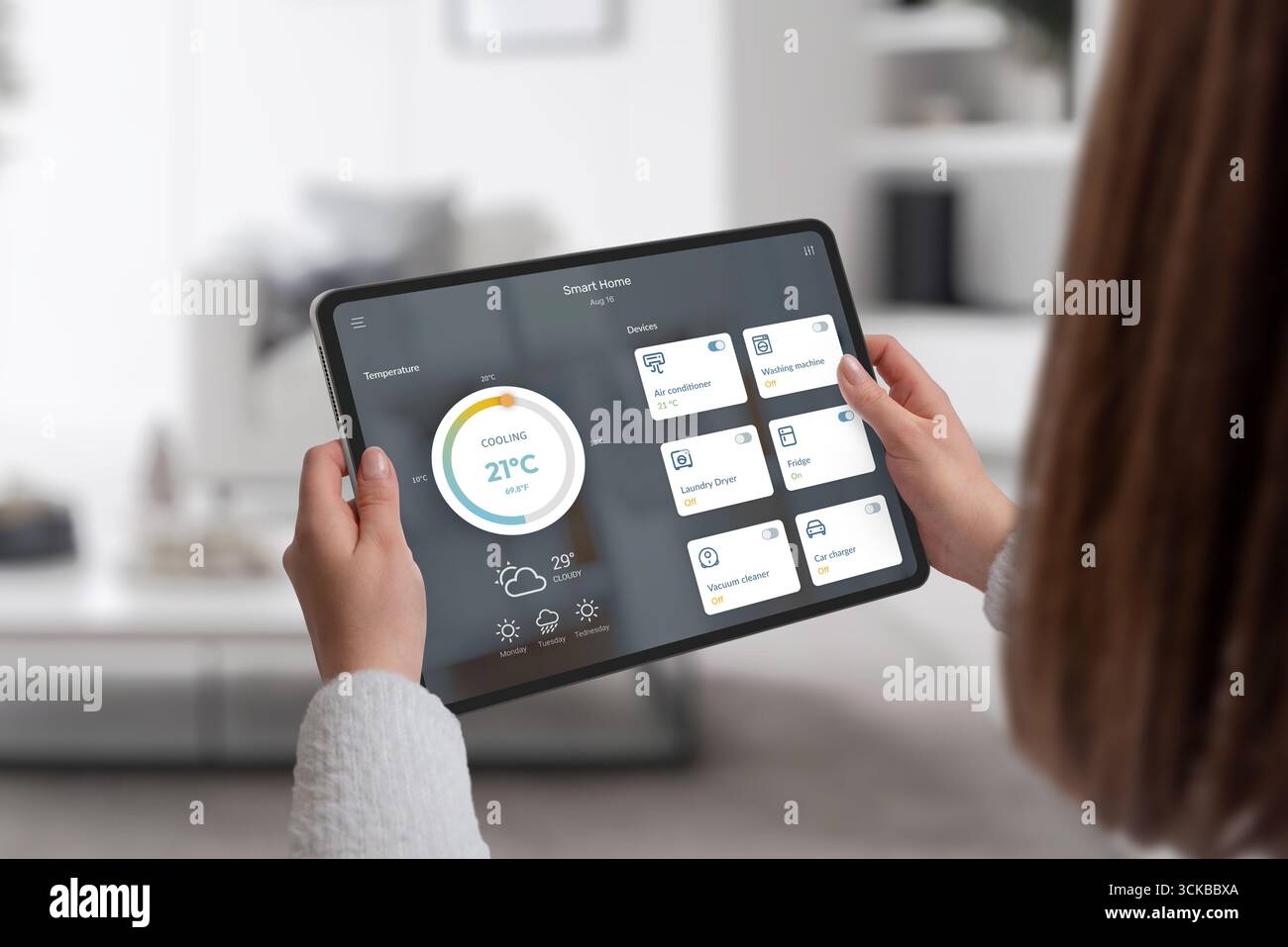 Person, die ein Tablet mit Smart-Home-Anwendung hält, um Klimaanlage, Waschmaschine und andere Haushaltsgeräte zu steuern Stockfoto