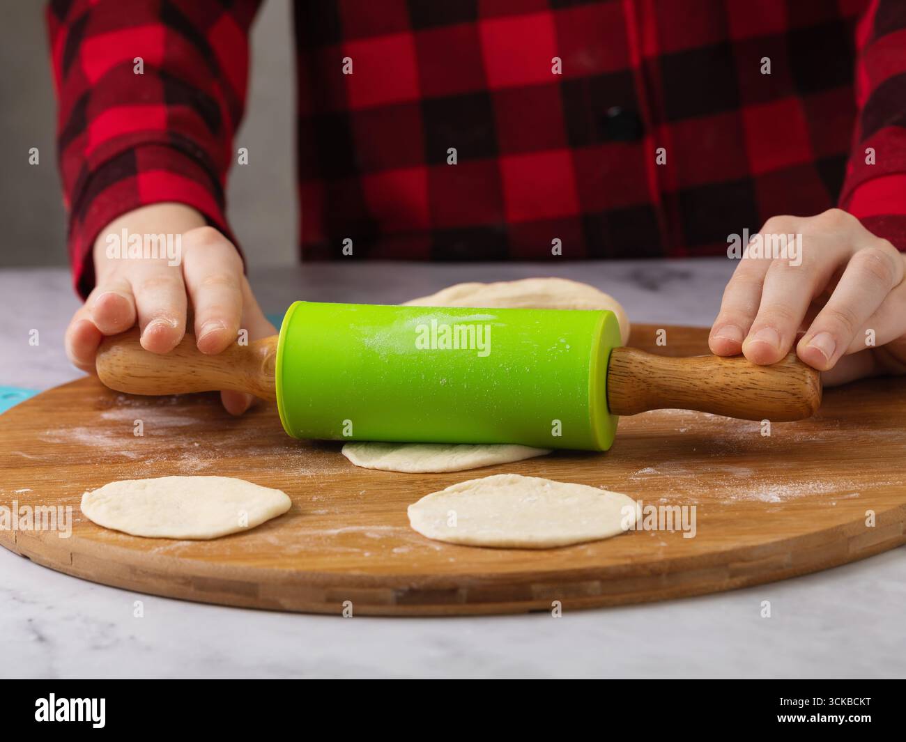 Ein Kind rollt den Teig mit einem Drehstift auf einem Holzbrett aus, Nahaufnahme Stockfoto
