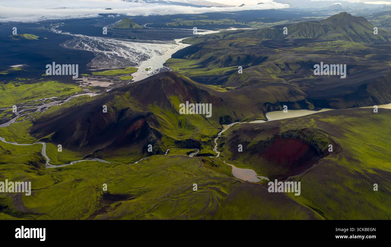 Aus der Vogelperspektive eines grünen Vulkankegels in Island, umgeben von dunklem Gelände, Flüssen, Seen, einem Gletscher und weitläufigen Ebenen im Hintergrund. Stockfoto