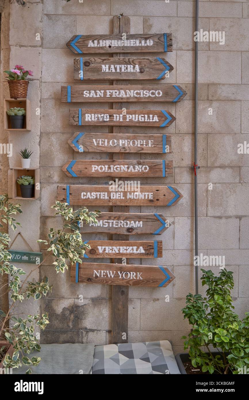 Dekorative hölzerne Wegweiser mit berühmten Städten und lokalen Städten auf einer Steinmauer mit Pflanzen und gemütlichem Dekor. Stockfoto