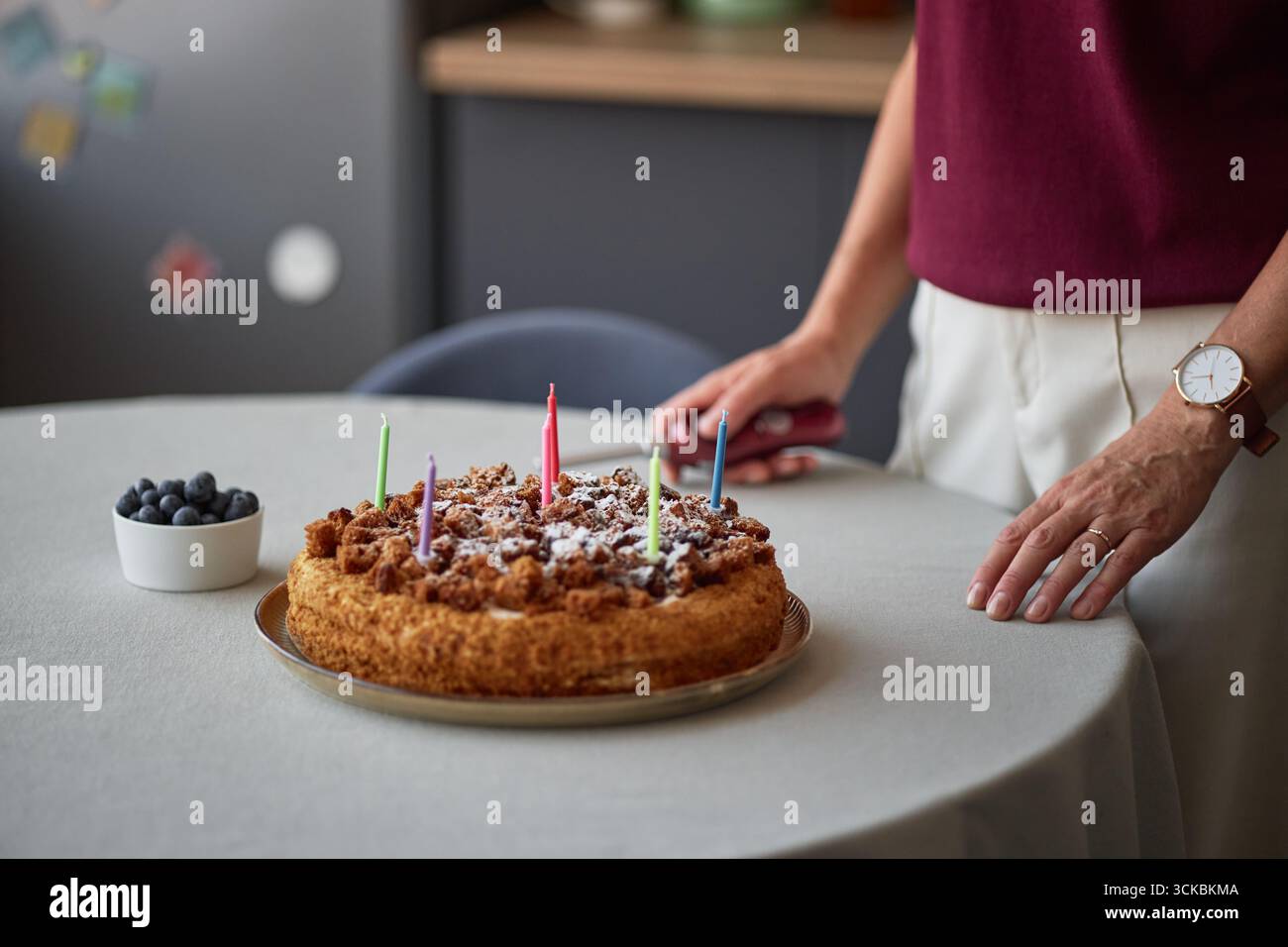 Frau mittleren Alters, die drinnen Geburtstagskuchen mit Kerzen zubereitet Stockfoto