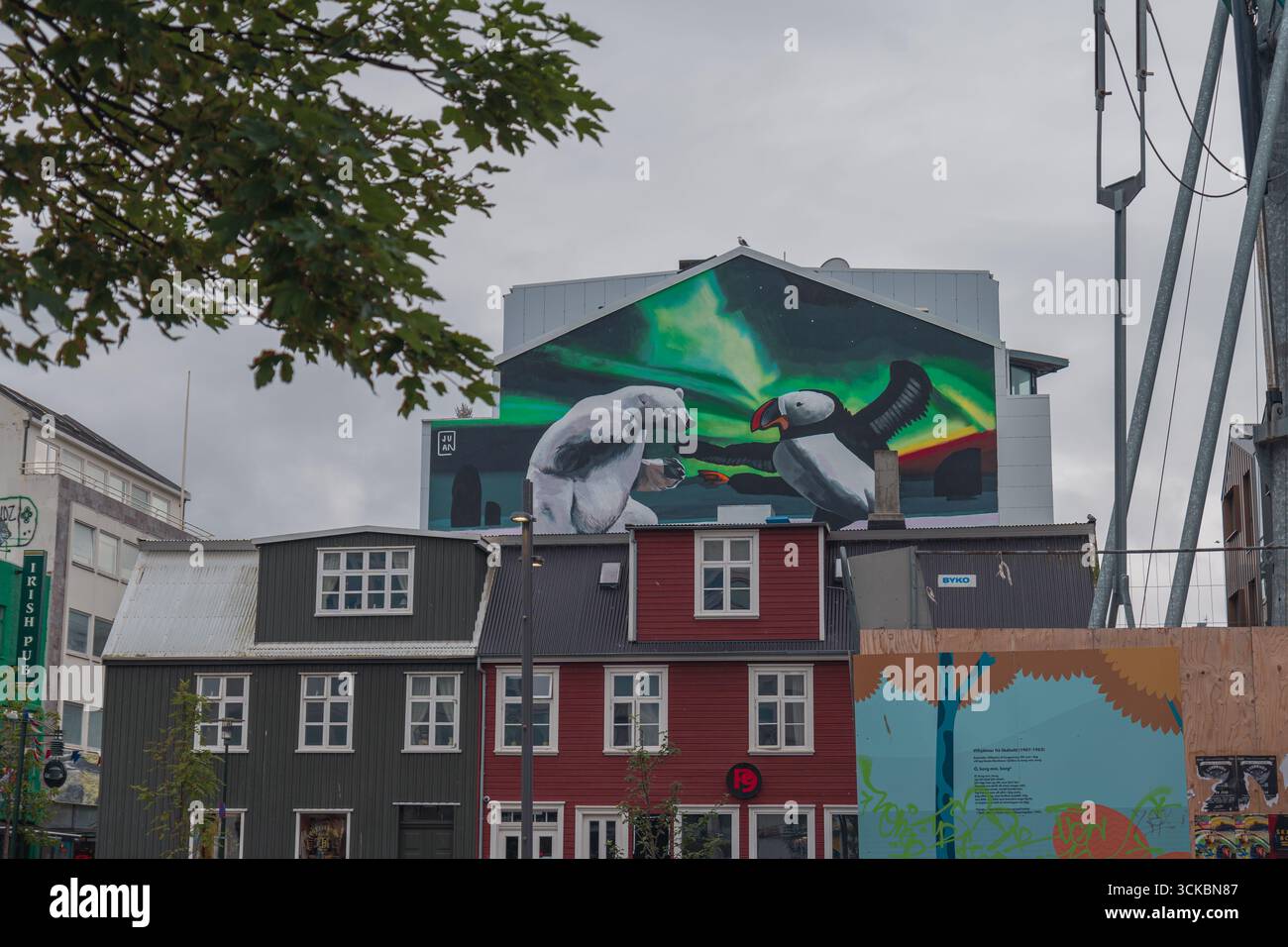 Lebendiges Wandbild in Reykjavik, Island, das einen Eisbären und Papageientaucher unter Nordlichtern zeigt. Traditionelle Architektur und urbane Elemente bilden den Rahmen für die sc Stockfoto