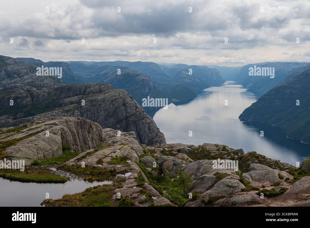 Blick auf Lysefjord in Norwegen, mit ruhigem Wasser, steilen felsigen Klippen, moosigen Stellen und einem bewölkten Himmel, der eine ruhige Atmosphäre schafft. Stockfoto