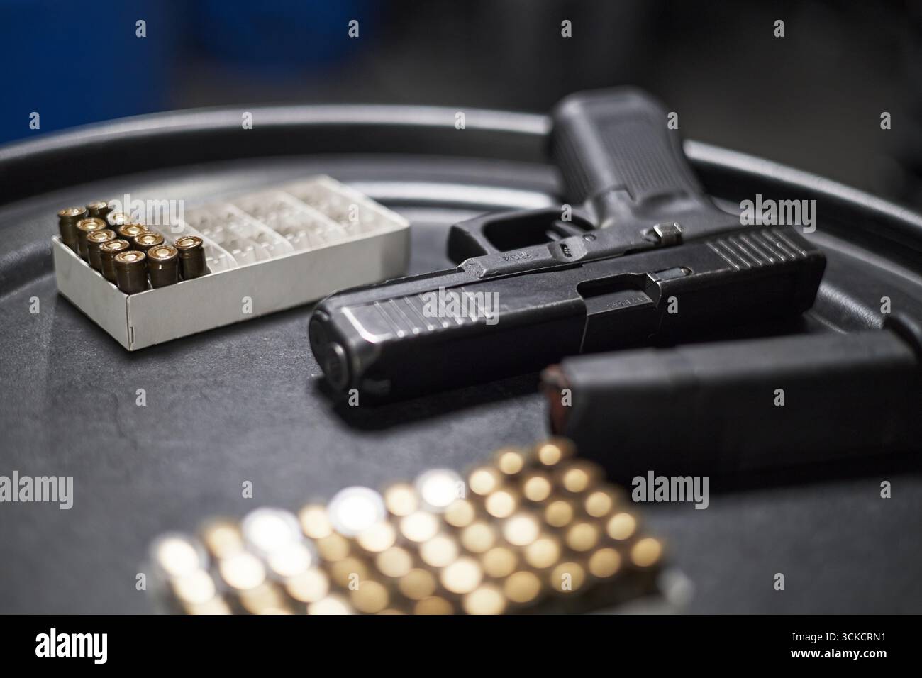Handfeuerwaffen auf runder schwarzer Oberfläche mit geladenem Magazin in der Nähe, Munitionskisten im Vorder- und Hintergrund, Fokus auf Schusswaffen und Kugeln, keine Menschen sichtbar Stockfoto