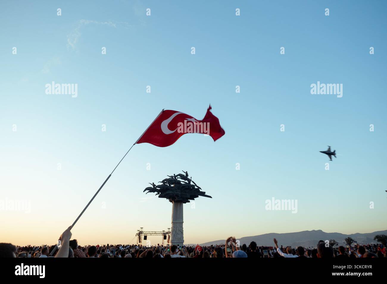 Izmir, Türkei - 9. September 2025: Foto einer winkenden türkischen Flagge am Himmel mit einem Jet-Überflug dahinter und einer Menschenmenge, die Fahnen hält, die auf Izmirs festgehalten wurden Stockfoto