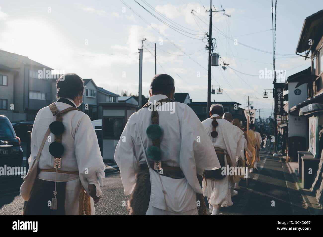 Mönche in weißen Gewändern laufen während des Tōka Ebisu Festivals in feierlicher Prozession durch eine Kyoto Straße, wobei rituelle Schärpen mit farbigen Pompons geschmückt sind Stockfoto