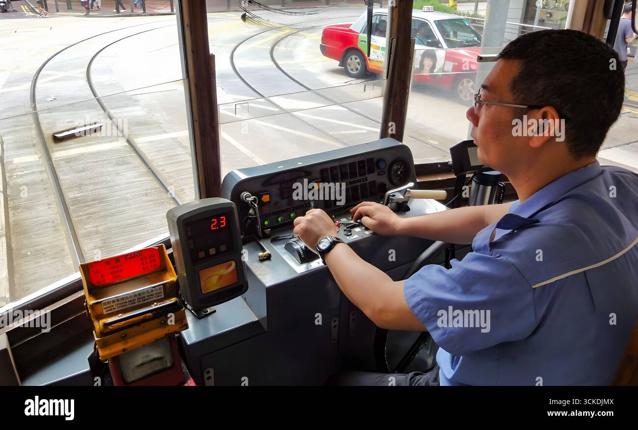 Straßenbahnfahrer, der eine Straßenbahn im alten Stil in Hongkong betreibt, vom Inneren des Cockpits aus gesehen. Stockfoto