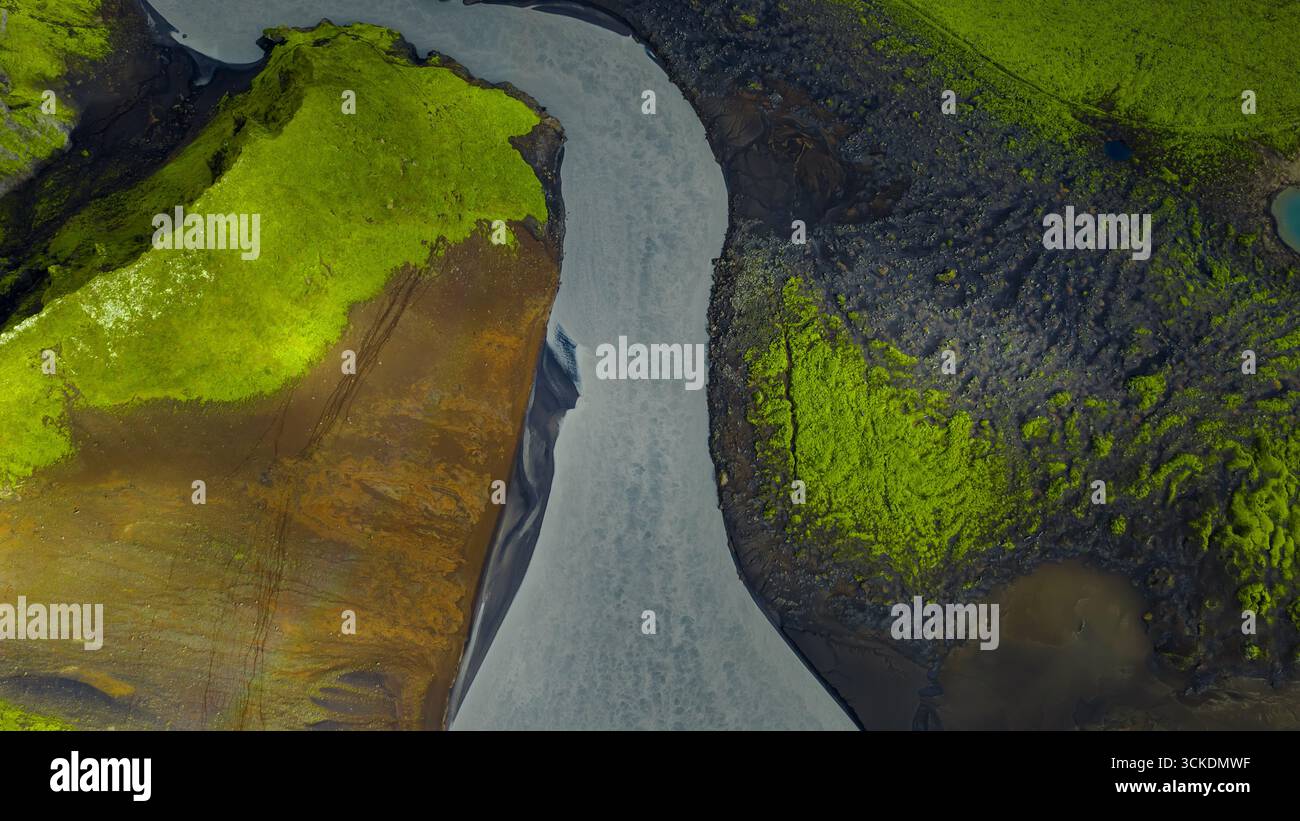 Aus der Vogelperspektive eines Gletscherflusses, der sich durch grünes moosbedecktes Gelände und dunklen vulkanischen Boden schlängelt, zeigt Islands einzigartige geologische Featur Stockfoto
