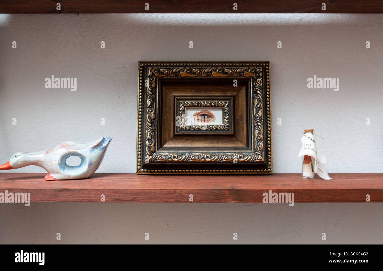 Dekoratives Regal mit gerahmter Augenkunst, Keramikente und kleiner Flasche. Stockfoto