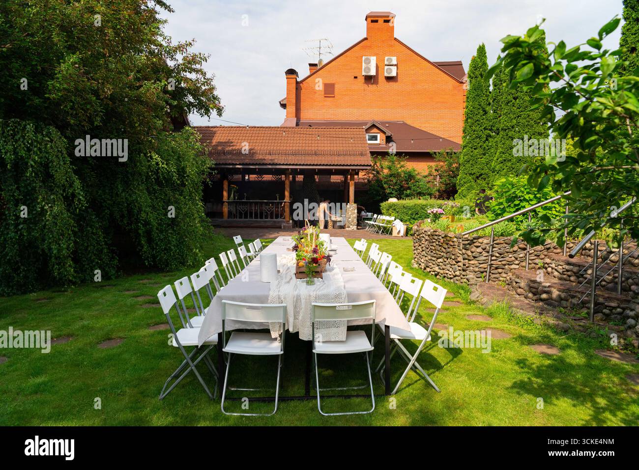 Hochzeitseinrichtung im Garten im Freien mit elegantem Tisch und rustikalem Backsteingebäude. Stockfoto