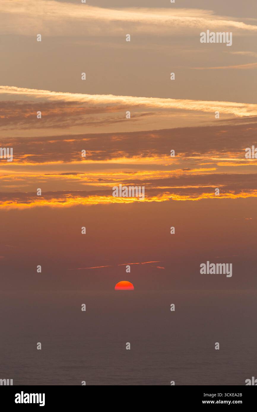 Sonnenaufgang/Sonnenaufgang im August in Aldeburgh, Suffolk. UK. Die Sonne geht aus dem Meer an einem leicht nebeligen, schönen Morgen mit blauem Himmel und Flugzeugdampfpfpfpfaden auf. (140) Stockfoto