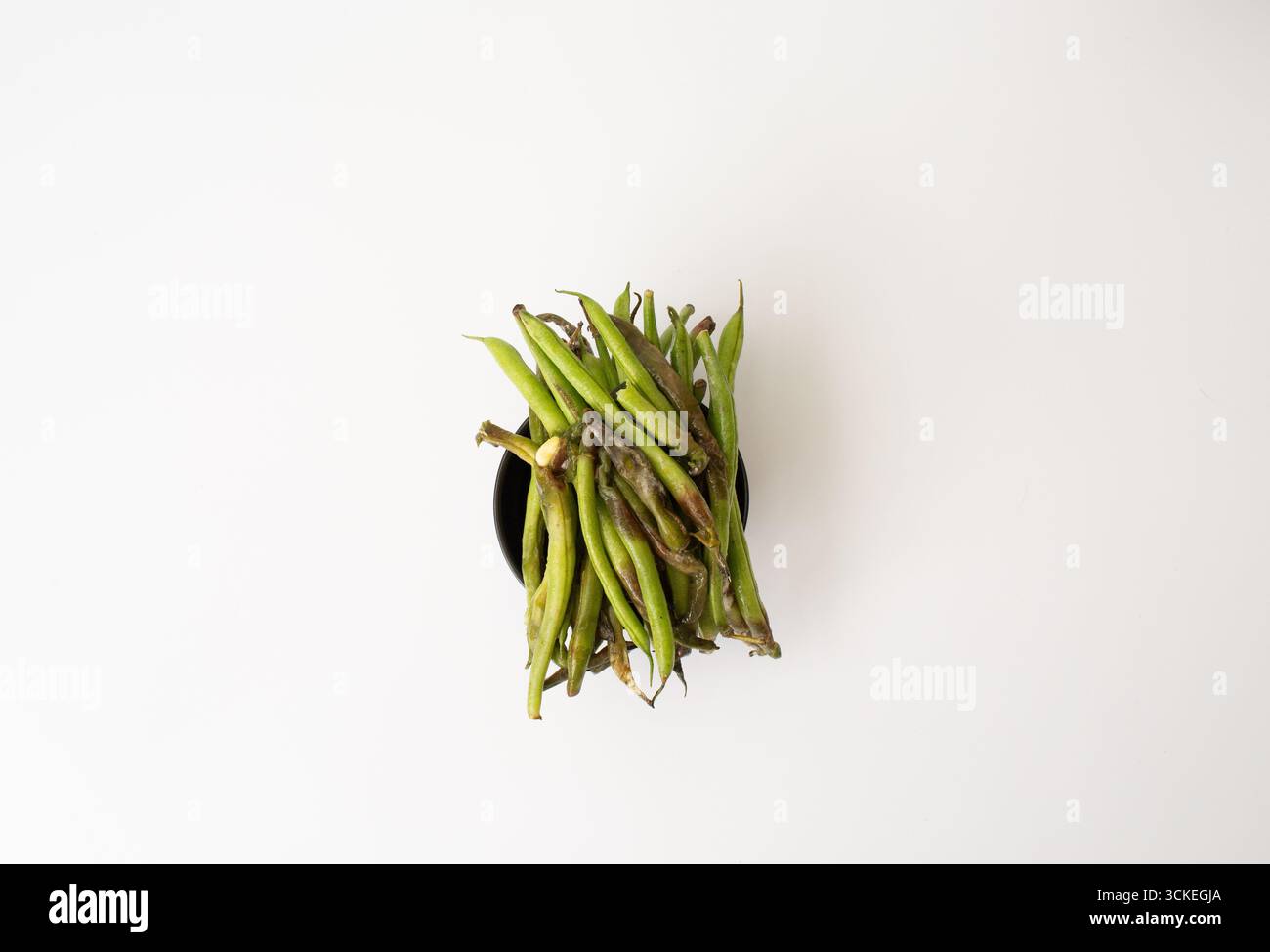 Nahaufnahme einer Schüssel mit verdorbenen, verfaulten grünen Bohnen, die Verfall und braune Flecken zeigen, isoliert auf weißem Hintergrund. Stockfoto