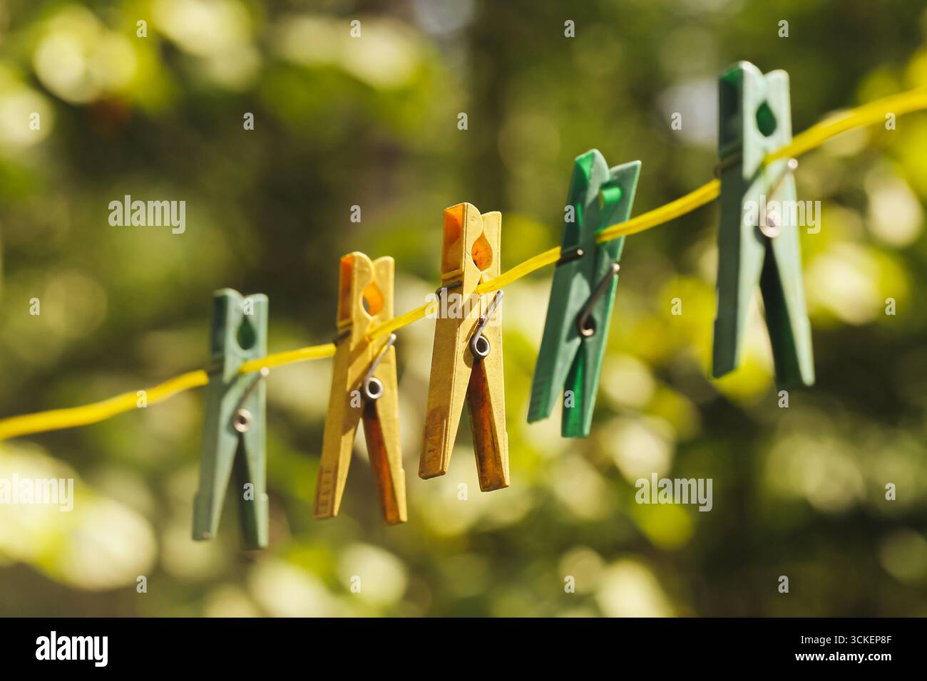 Bunte Kleiderschalen hängen an der Wäscheleine. Kunststoffhalterungen am Seil vor verschwommenem natürlichen Hintergrund. Detailansicht des Haushalts. Kleidung trocknen. Stockfoto