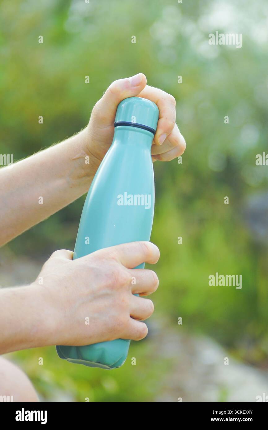 Die Hände des Mannes, die Wasserflasche im Park halten. Konzept der achtsamen Hydration, Wellness-Routine, Selbstpflegeritual, Gesundheitsbewusstsein, Öko-Lebensstil Stockfoto