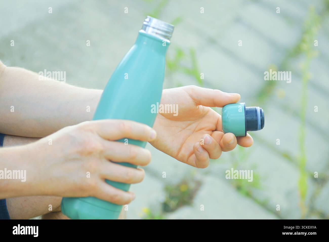 Person, die im Begriff ist, mit wiederverwendbarer Thermoflasche aus Metall im Außenbereich zu hydrieren. Trinkzubereitung und Aufnahme von Trinkmomenten. Durstlinderung Stockfoto