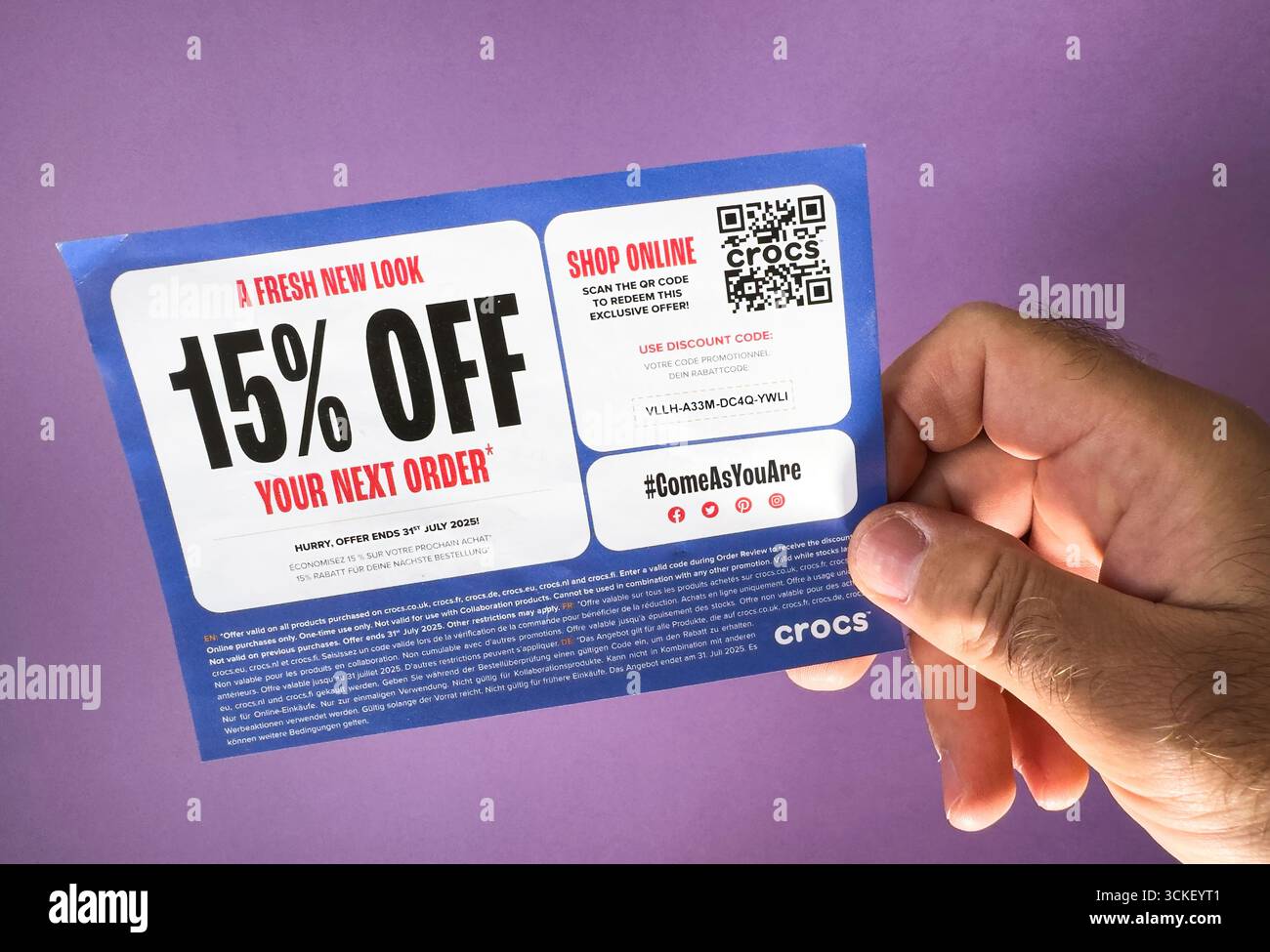 Paris, Frankreich - 2. September 2025: Nahaufnahme einer Hand, die eine Crocs-Rabattgutscheinkarte mit Werbetext und QR-Code vor violettem Hintergrund hält Stockfoto