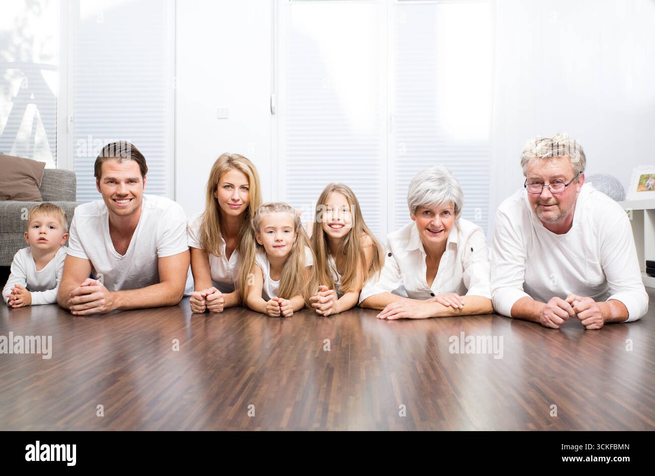 Familie mit drei Kindern, Oma und Opa sitzen am Wohnzimmertisch Stockfoto