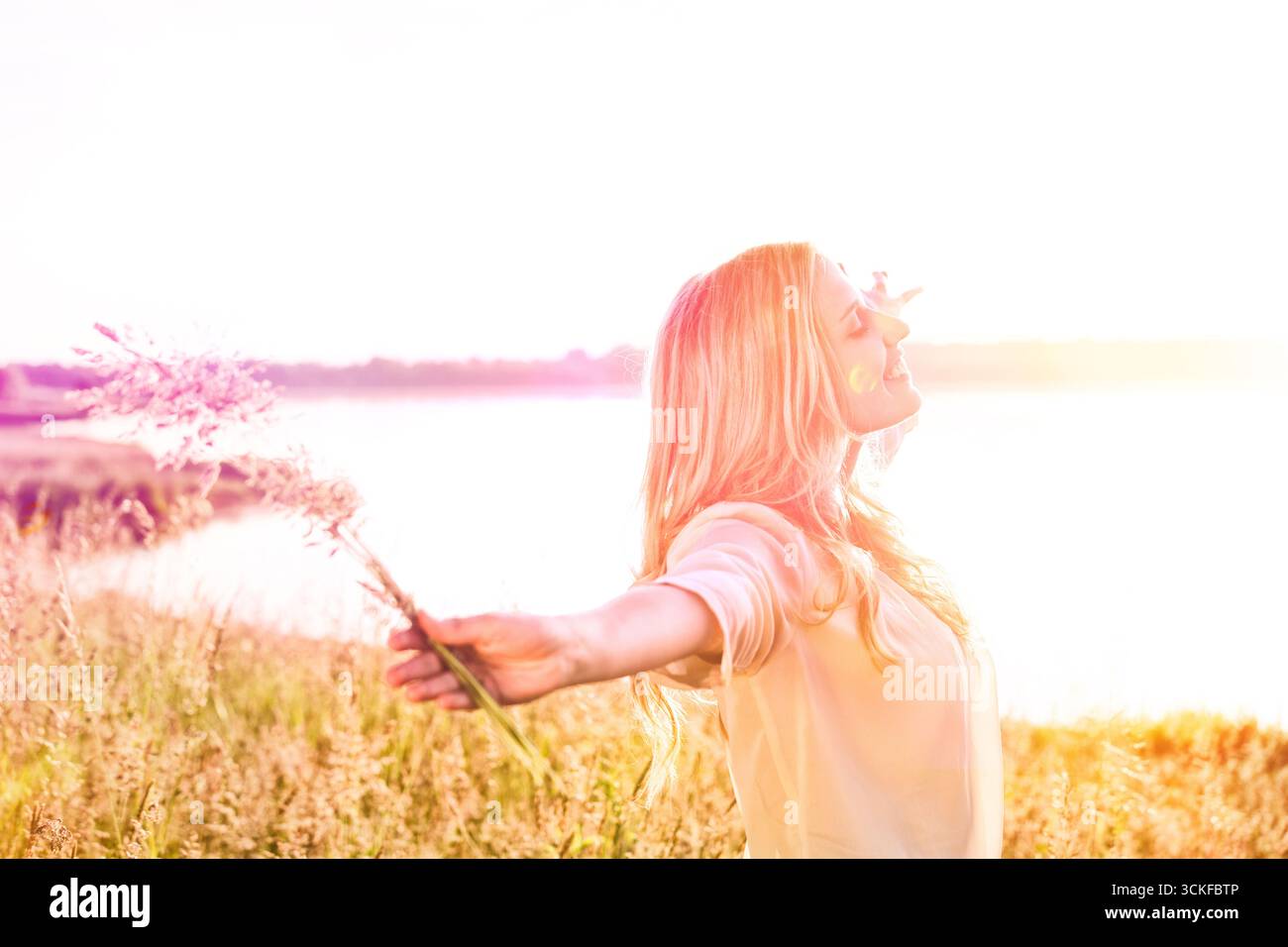 Eine junge Frau, die ihre Arme ausstreckt und die Sonne genießt Stockfoto