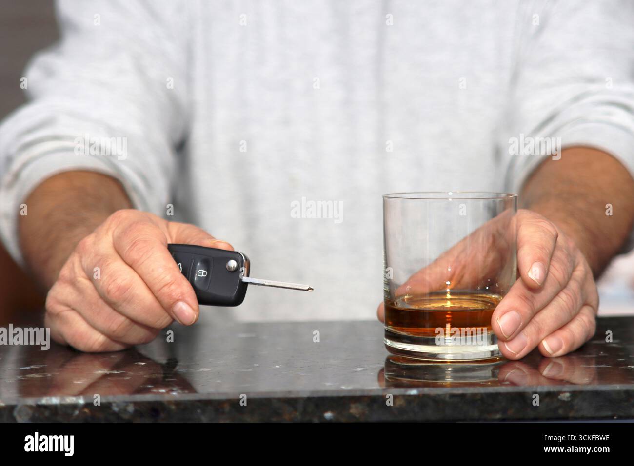 Autoschlüssel in der einen Hand, ein Glas Whisky in der anderen, symbolisches Bild des Getränkefahrens Stockfoto