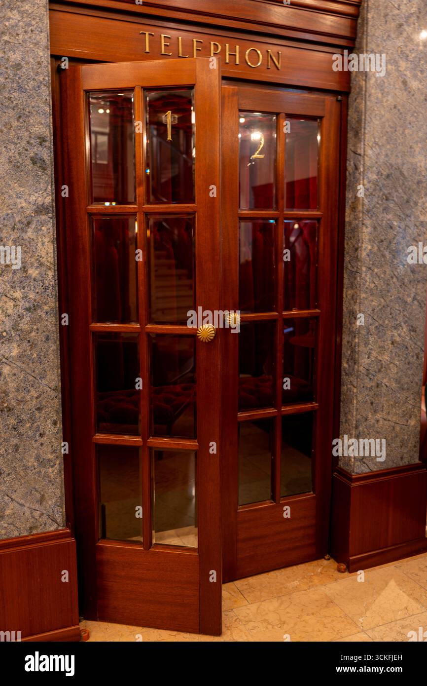 Detaillierte Ansicht einer luxuriösen Vintage-Telefonkabine mit poliertem Holz, Glaseinsätzen und Messingknöpfen – perfekt für Architektur, Nostalgie, Stockfoto
