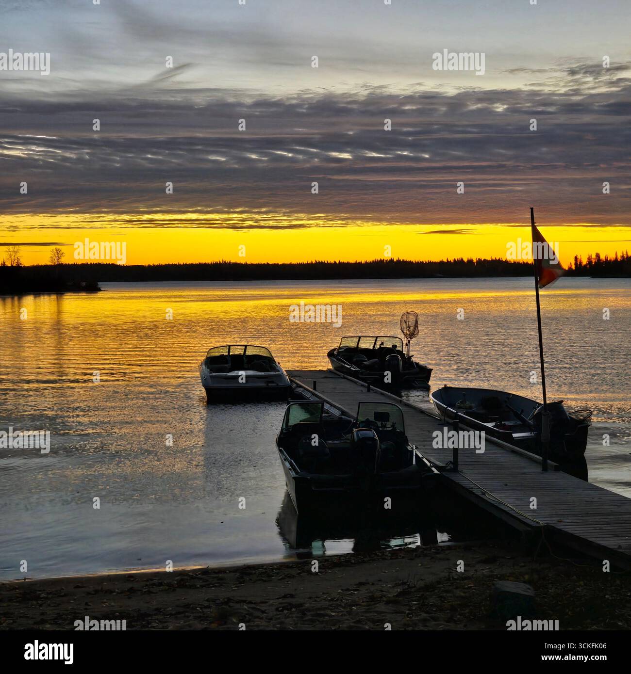 'Farbenfroher Sonnenuntergang über einem ruhigen See mit Booten an der Küste und Wald in der Ferne.' - Smartphone-aufgenommenes Stockfoto