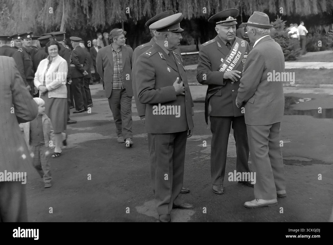Ein Treffen von Veteranen des Großen Vaterländischen Krieges und Offizieren der sowjetischen Armee während eines Siegtages in Sloviansk in den 1970er Jahren Dieses ehrliche Foto zeigt ein ernsthaftes Gespräch zwischen drei Männern – zwei in gekleideten Militäruniformen mit Medaillen und einer in Zivilkleidung. Die Szene dient als eindrucksvolles dokumentarisches Zeugnis für die Kameradschaft, die Bewahrung des Kriegsgedächtnisses und den besonderen, geehrten Status, den Veteranen in der sowjetischen Gesellschaft während der Stagnation der Breschnew-Ära innehatten und ihre Rolle als lebendige Symbole der Geschichte widerspiegeln Stockfoto