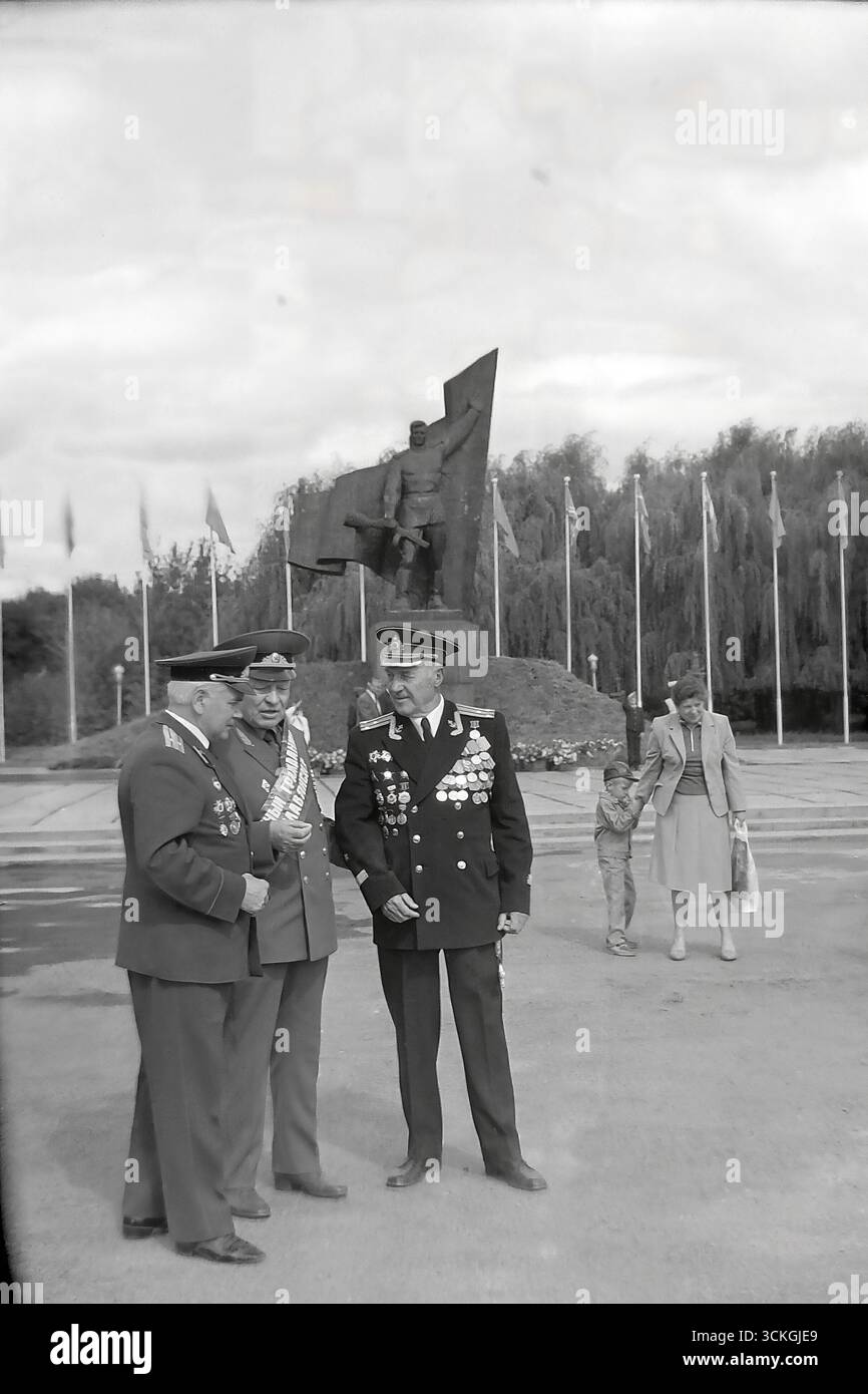 Ein feierliches Porträt von drei hochrangigen Veteranen des Großen Vaterländischen Krieges, die in ihren vollen Uniformen mit zahlreichen Auszeichnungen festgehalten wurden, als sie in den 1970er Jahren vor dem Denkmal für den Befreiungssoldaten in Sloviansk posierten Dieses eindrucksvolle Foto vermittelt perfekt die Atmosphäre einer Feier zum Siegtag und präsentiert die Veteranen als lebendige Symbole des Sieges und die Hüter des historischen Gedächtnisses der sowjetischen Gesellschaft während der Stagnation der Breschnew-Ära, die den offiziellen Kult des Kriegsheld verkörpert Stockfoto