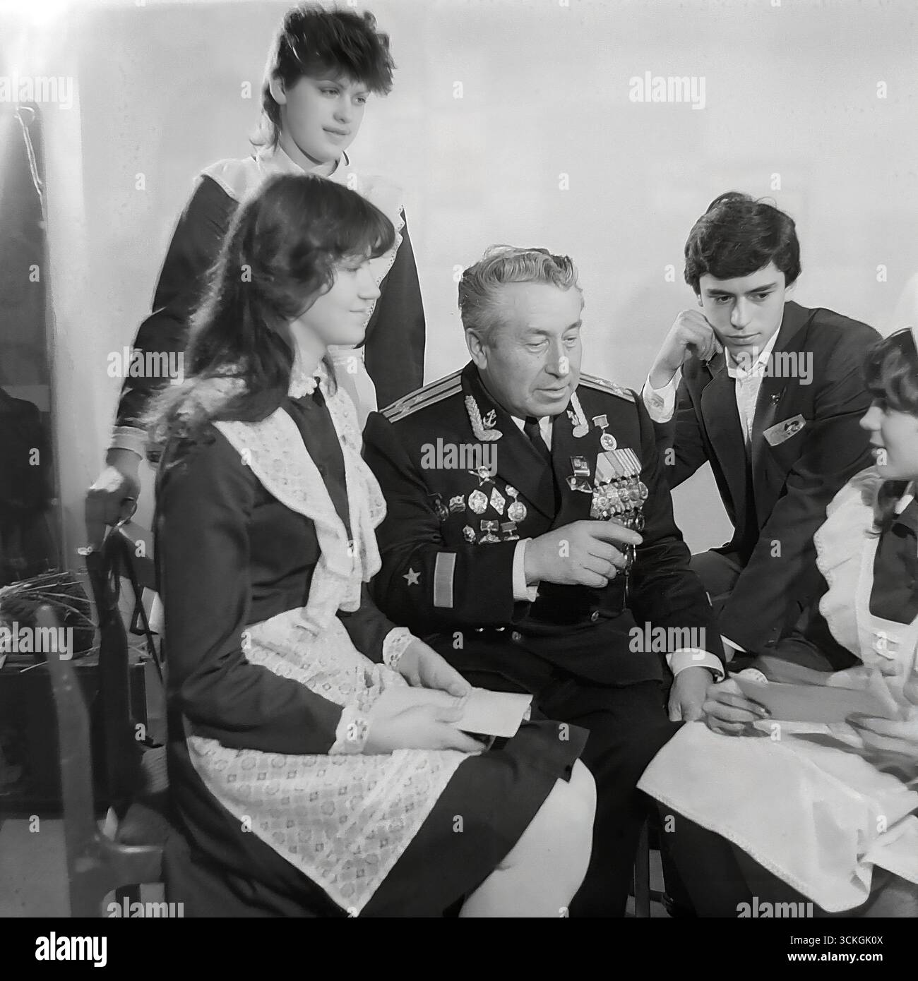 Ein "Generationentreffen" an der Sekundarschule Nr. 12 in Sloviansk Ende der 1970er Jahre Der Voenruk (Militärlehrer) der Schule, ein dekorierter Marineveteran in seiner vollen Uniform mit Medaillen, führt eine „Courage-Lektion“ für High School-Schüler durch. Die Schüler, gekleidet in Standard-sowjetische Schuluniformen mit einem Komsomol-Abzeichen, hören sich seine Kriegsgeschichten an. Dieses Bild ist symbolisch für das umfassende System patriotischer Jugenderziehung, das während der Breschnew-Ära ein Eckpfeiler der Gesellschaft in der UdSSR war Stockfoto