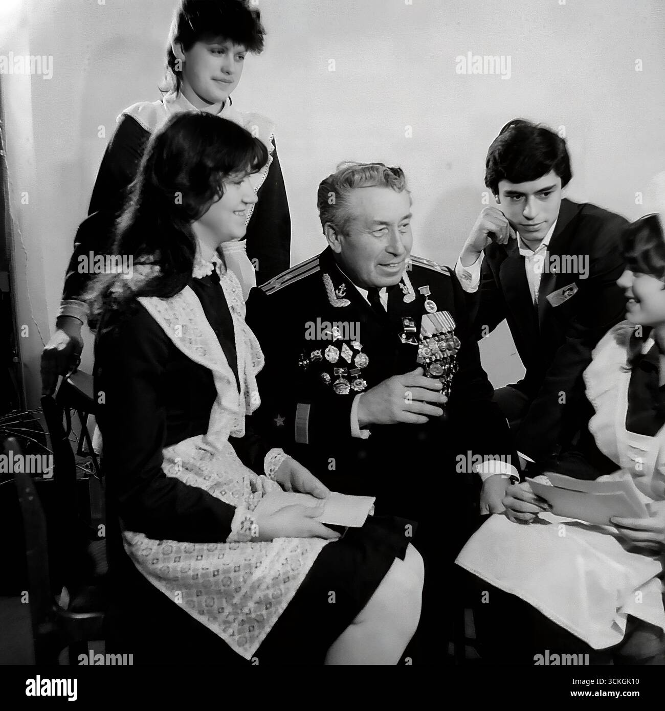 Ein "Generationentreffen" an der Sekundarschule Nr. 12 in Sloviansk Ende der 1970er Jahre Der Voenruk (Militärlehrer) der Schule, ein dekorierter Marineveteran in seiner vollen Uniform mit Medaillen, führt eine „Courage-Lektion“ für High School-Schüler durch. Die Schüler, gekleidet in Standard-sowjetische Schuluniformen mit einem Komsomol-Abzeichen, hören sich seine Kriegsgeschichten an. Dieses Bild ist symbolisch für das umfassende System patriotischer Jugenderziehung, das während der Breschnew-Ära ein Eckpfeiler der Gesellschaft in der UdSSR war Stockfoto
