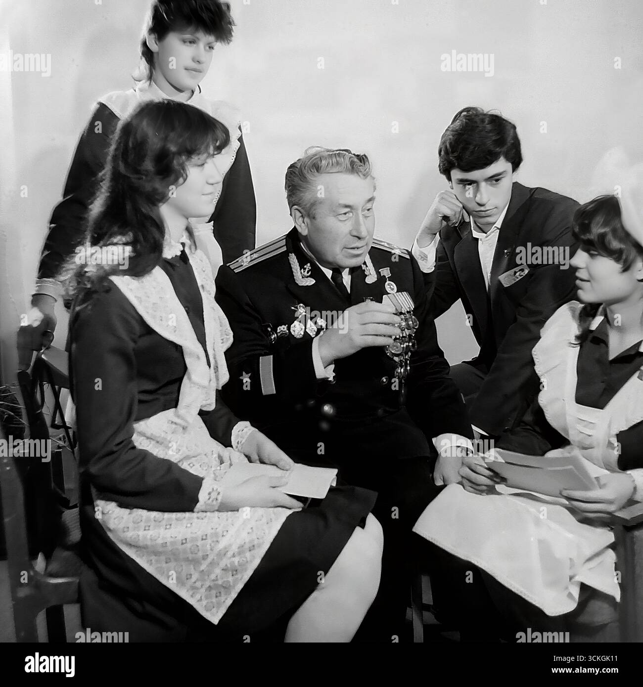 Ein "Generationentreffen" an der Sekundarschule Nr. 12 in Sloviansk Ende der 1970er Jahre Der Voenruk (Militärlehrer) der Schule, ein dekorierter Marineveteran in seiner vollen Uniform mit Medaillen, führt eine „Courage-Lektion“ für High School-Schüler durch. Die Schüler, gekleidet in Standard-sowjetische Schuluniformen mit einem Komsomol-Abzeichen, hören sich seine Kriegsgeschichten an. Dieses Bild ist symbolisch für das umfassende System patriotischer Jugenderziehung, das während der Breschnew-Ära ein Eckpfeiler der Gesellschaft in der UdSSR war Stockfoto