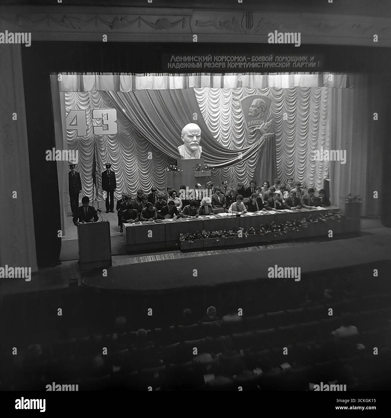 Eine feierliche Sitzung der 43. Komsomol-Konferenz in Sloviansk, fotografiert in den späten 1970er Jahren Die Bühne des Kulturpalastes ist mit einer Leninbüste und einem Slogan über den Komsomol als Reserve der Partei dekoriert, mit Delegierten auf einem Präsidium und einem Redner auf dem Podium. Dieses Foto dient als dokumentarischer Beweis für das hoch ritualisierte sozio-politische Leben in der UdSSR während der Stagnation der Breschnew-Ära und erfasst die formale Atmosphäre der offiziellen Jugendpolitik Stockfoto