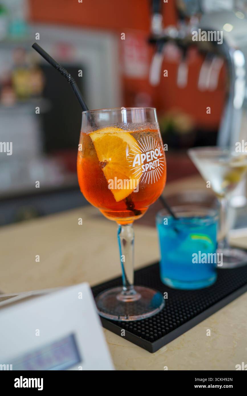 Crema, Italien - 25. August 2025 erfrischender Aperitif-Cocktail in leuchtendem Orange, garniert mit frischem Zitrusstück und dunklem Strohhalm an einem Bartheken mit Soft Stockfoto