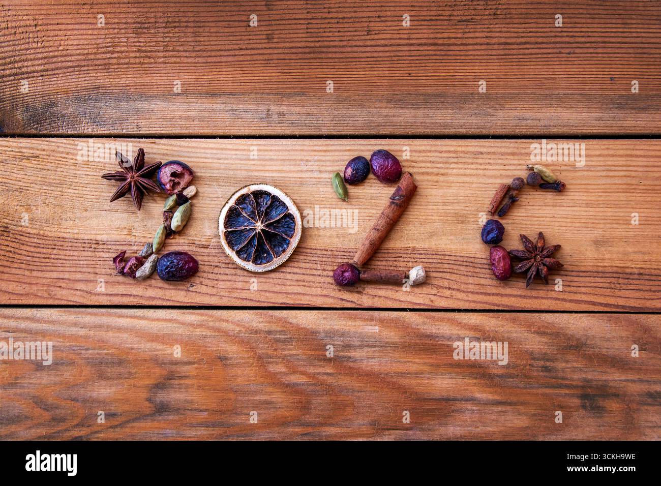 2026 geschrieben mit Weihnachtsgewürzen und getrocknetem Essen auf hölzernem Hintergrund, Neujahrsfeiertagskarte Stockfoto