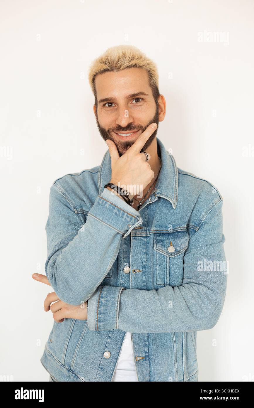 Junger Mann posiert selbstbewusst mit einem Lächeln und einer stylischen Jeansjacke Stockfoto