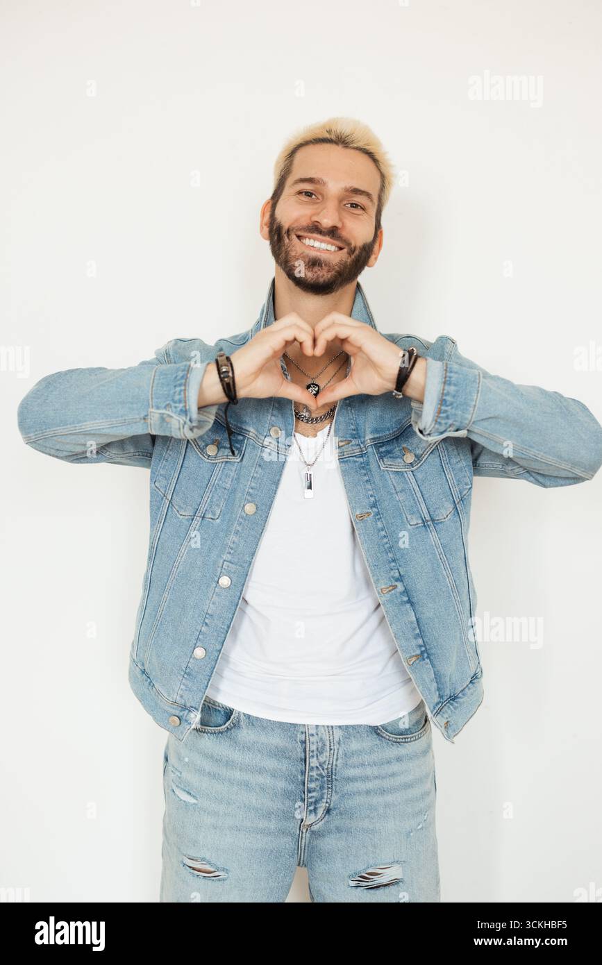 Lächelnder Mann, der Herzgeste mit Händen in lässigem Outfit zeigt Stockfoto