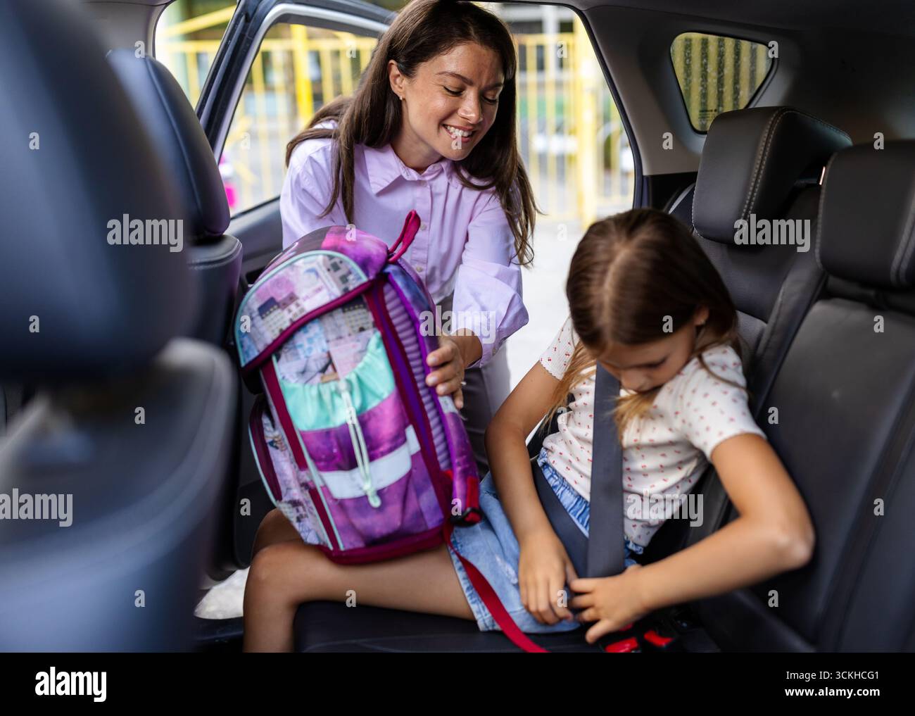 Mutter hilft der Tochter, sich vor der Schule mit dem Rucksack auf dem Rücksitz anzuschnallen Stockfoto