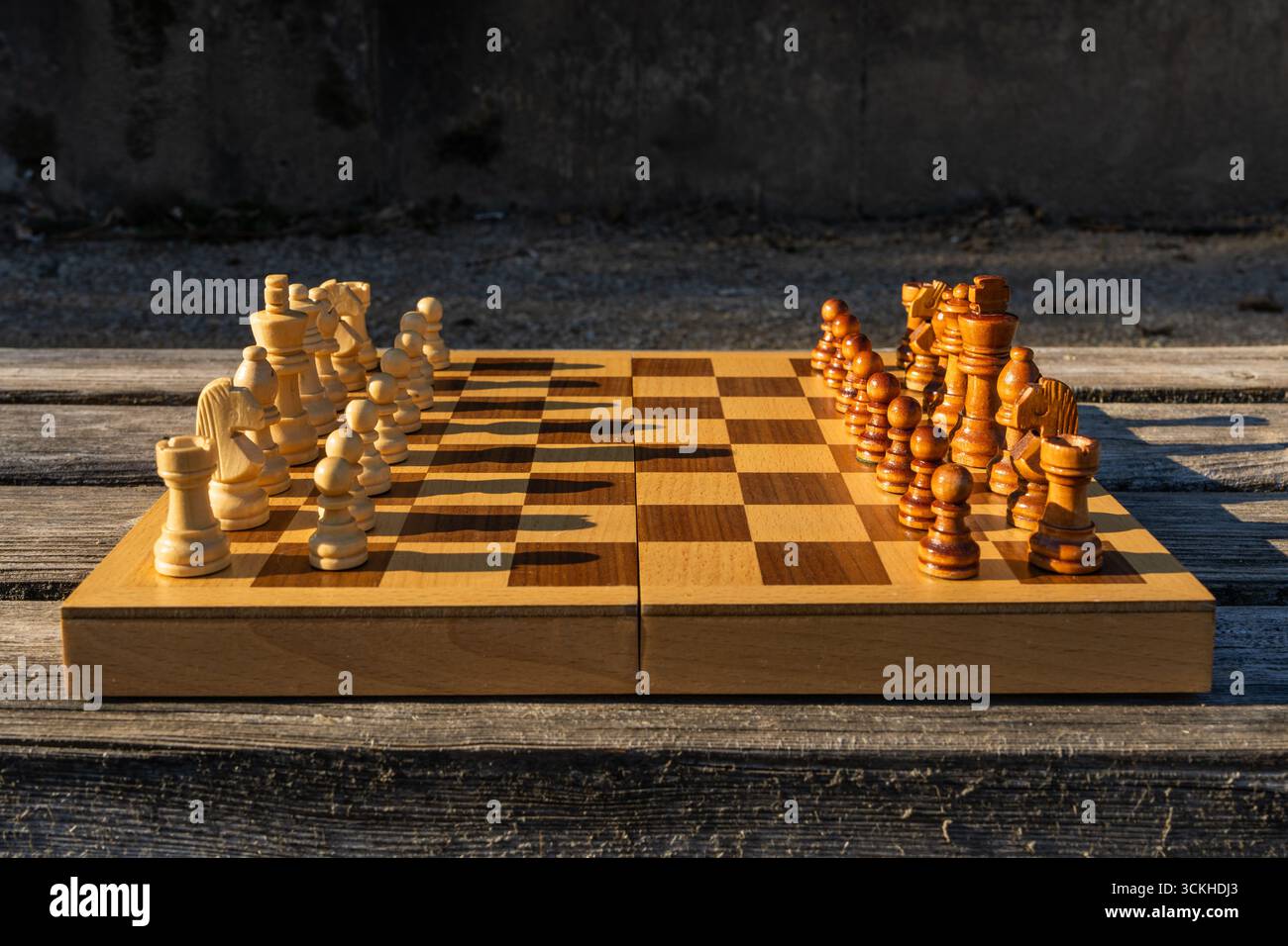 Schachbrett mit angeordneten Stücken auf Holzbank im Stadtpark. Outdoor-Setup für strategisches Spiel bei Tageslicht, symbolisiert Freizeit, Intelligenz, R Stockfoto