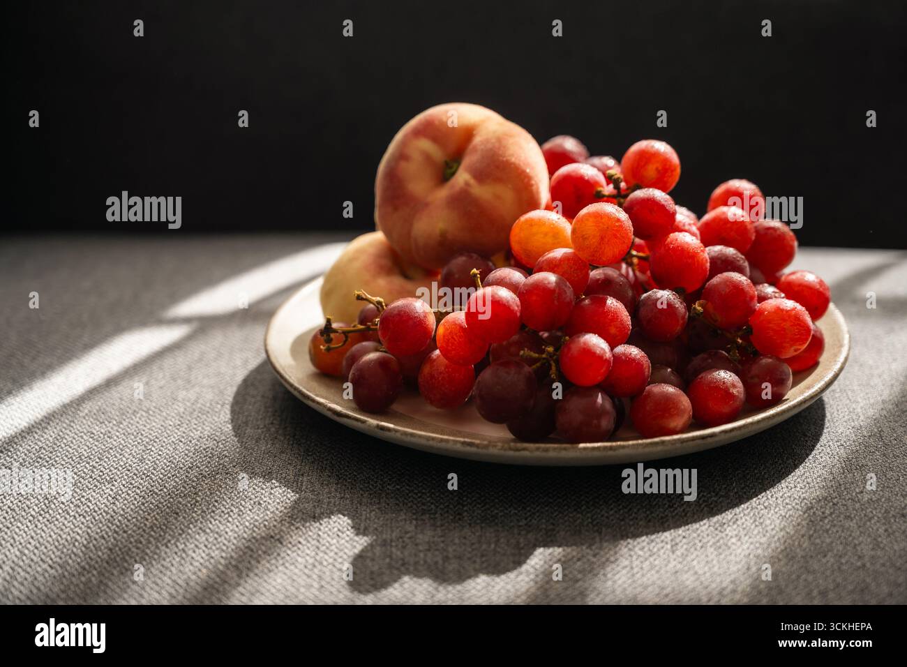 Obst auf einem Teller, Sonnenlicht. Pfirsiche und grüne Trauben Stockfoto