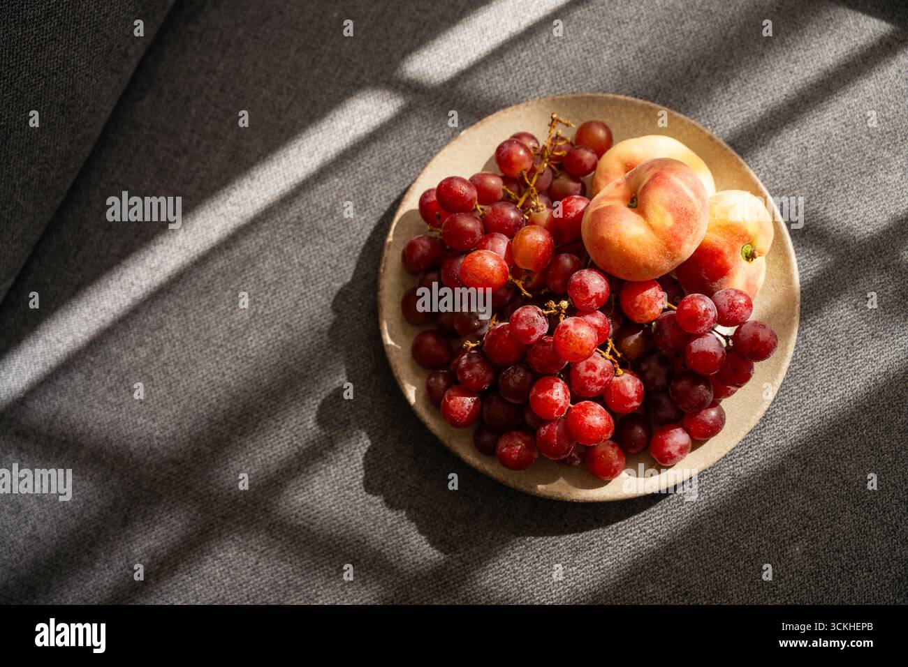 Obst auf einem Teller, Sonnenlicht. Pfirsiche und grüne Trauben. Stockfoto