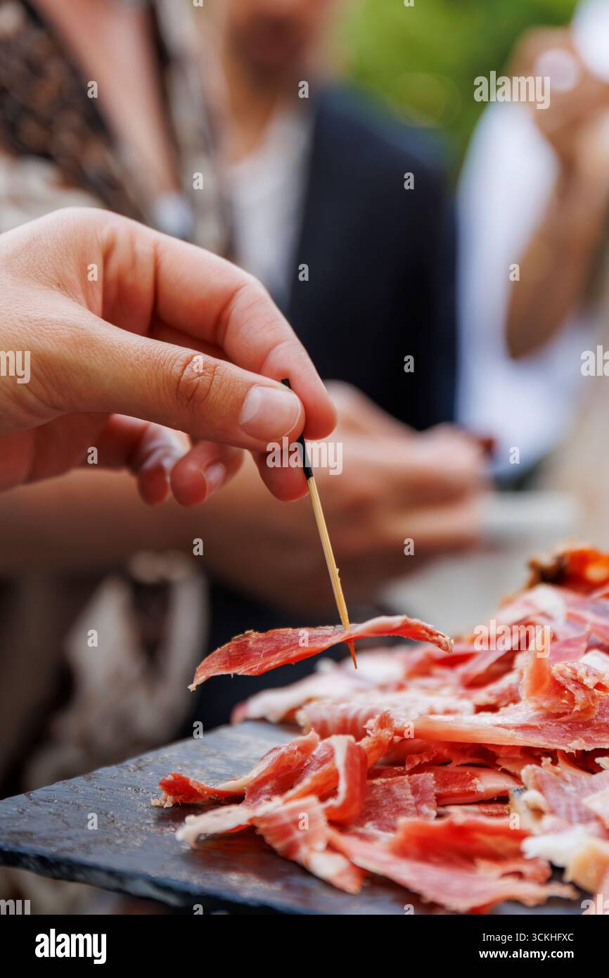Ein Gast serviert sich ein Stück iberischen Schinken während einer After Work Party Stockfoto